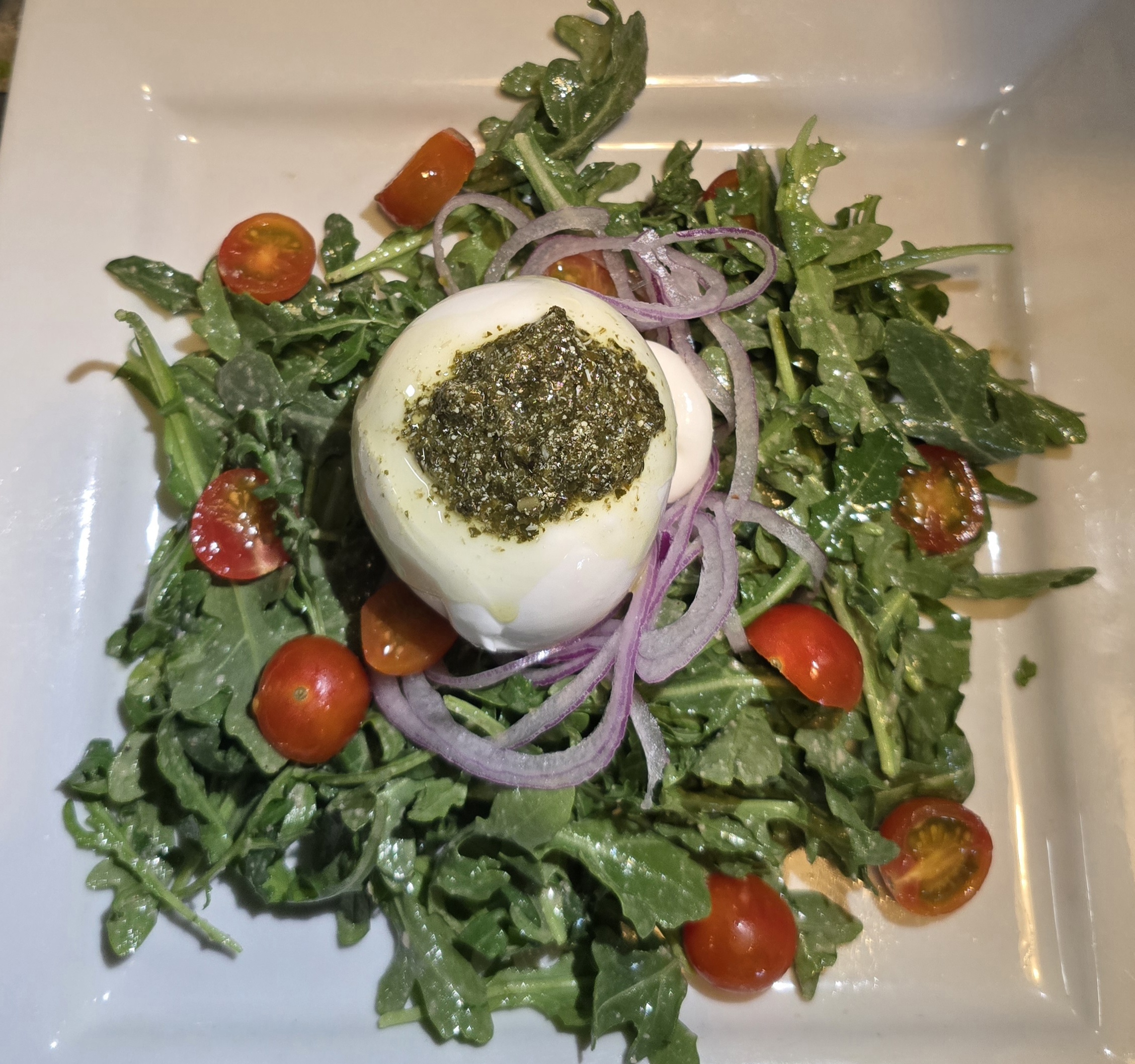 Fresh Burrata Salad topped with pesto on greens.